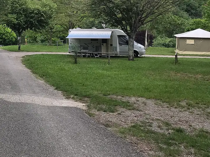 Camping-car avec store déployé sur un emplacement herbeux en bordure d'allée