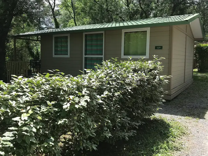 Mobile-home numéroté avec terrasse couverte, entouré de haies