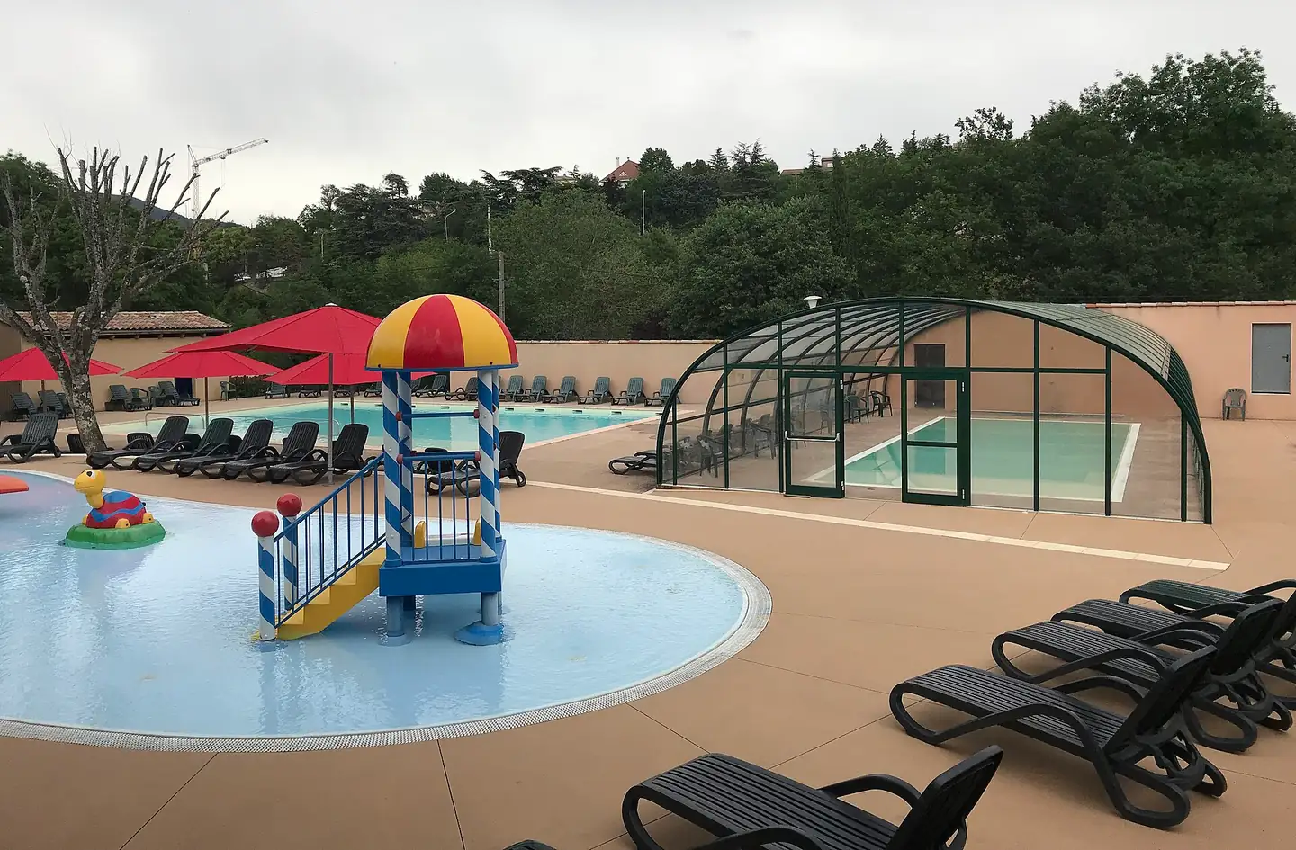 Pataugeoire avec jeux d'eau pour enfants, piscine extérieure et bassin couvert sous un dôme vitré dans un camping d'Ardèche